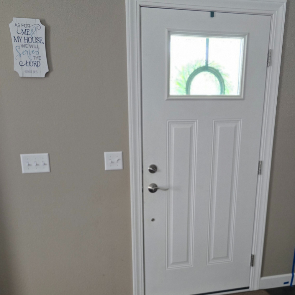 White door with a small window and decorative glass, next to a gray wall with a sign.