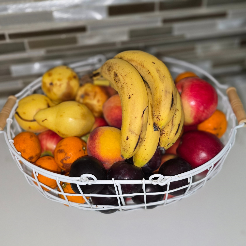 Fruit basket with bananas, apples, oranges, and plums on a kitchen counter.