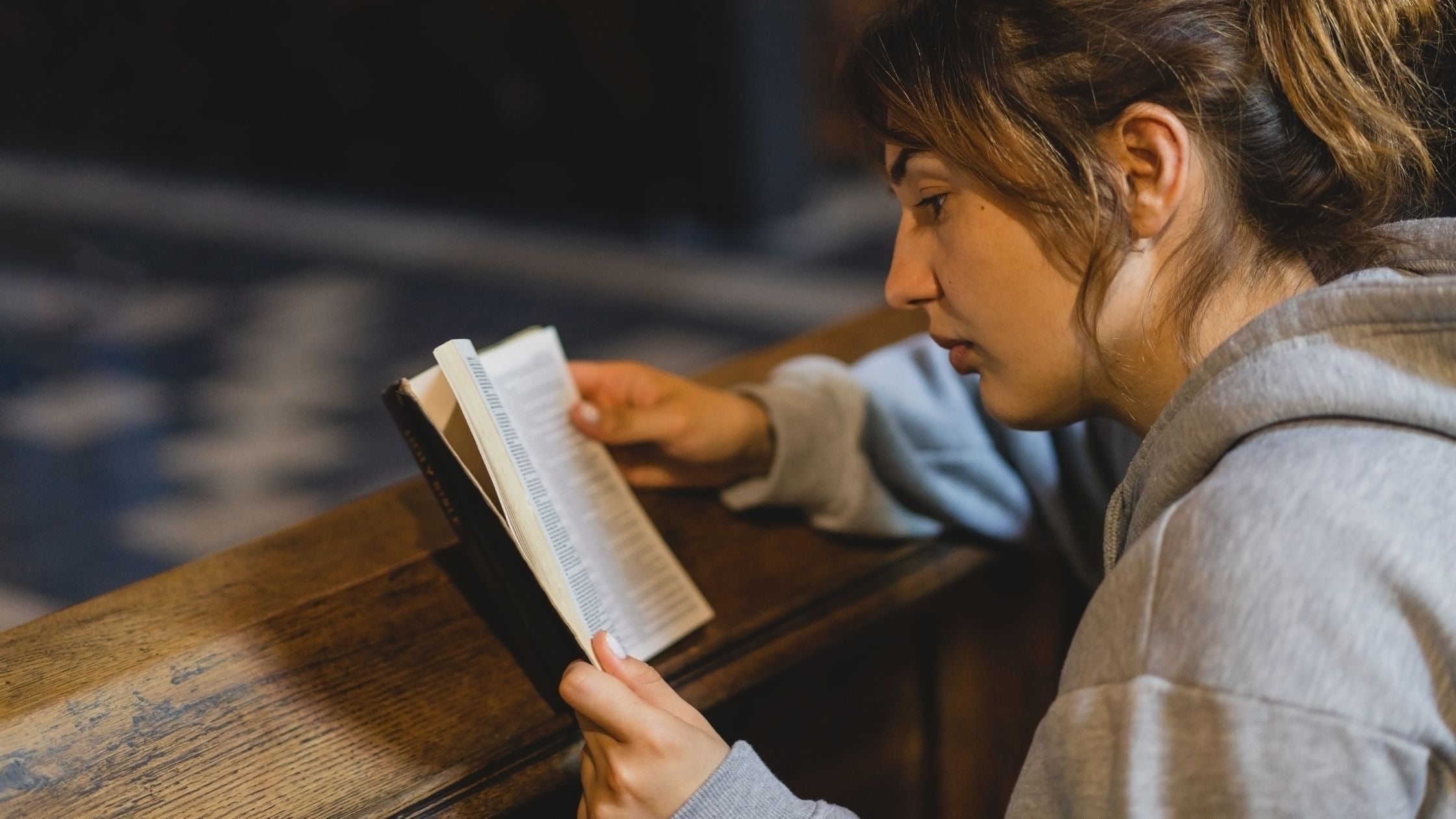Woman reading the Bible book in a pew in a church.